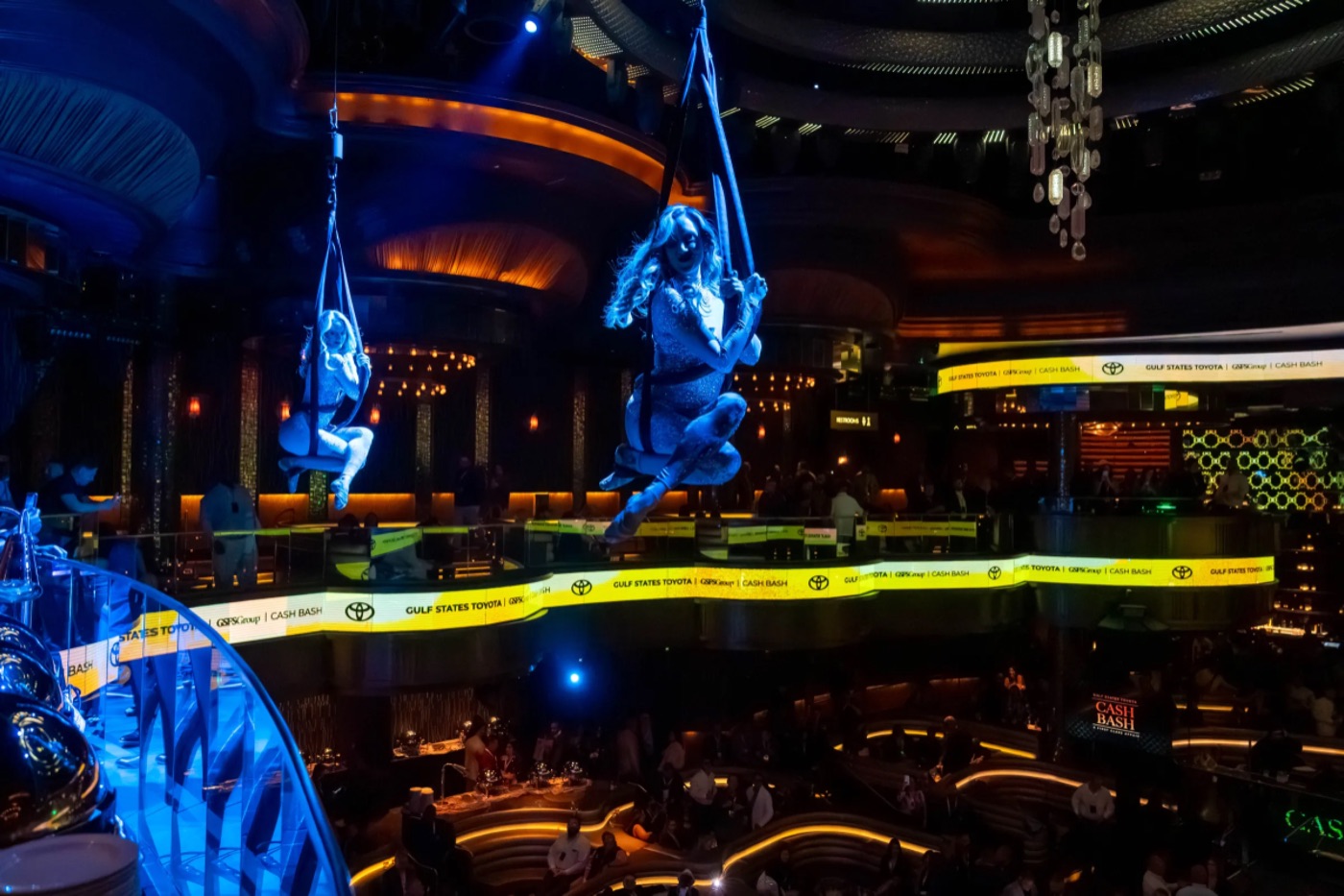 Aerial performers suspended above a crowd in a blue-lit venue.