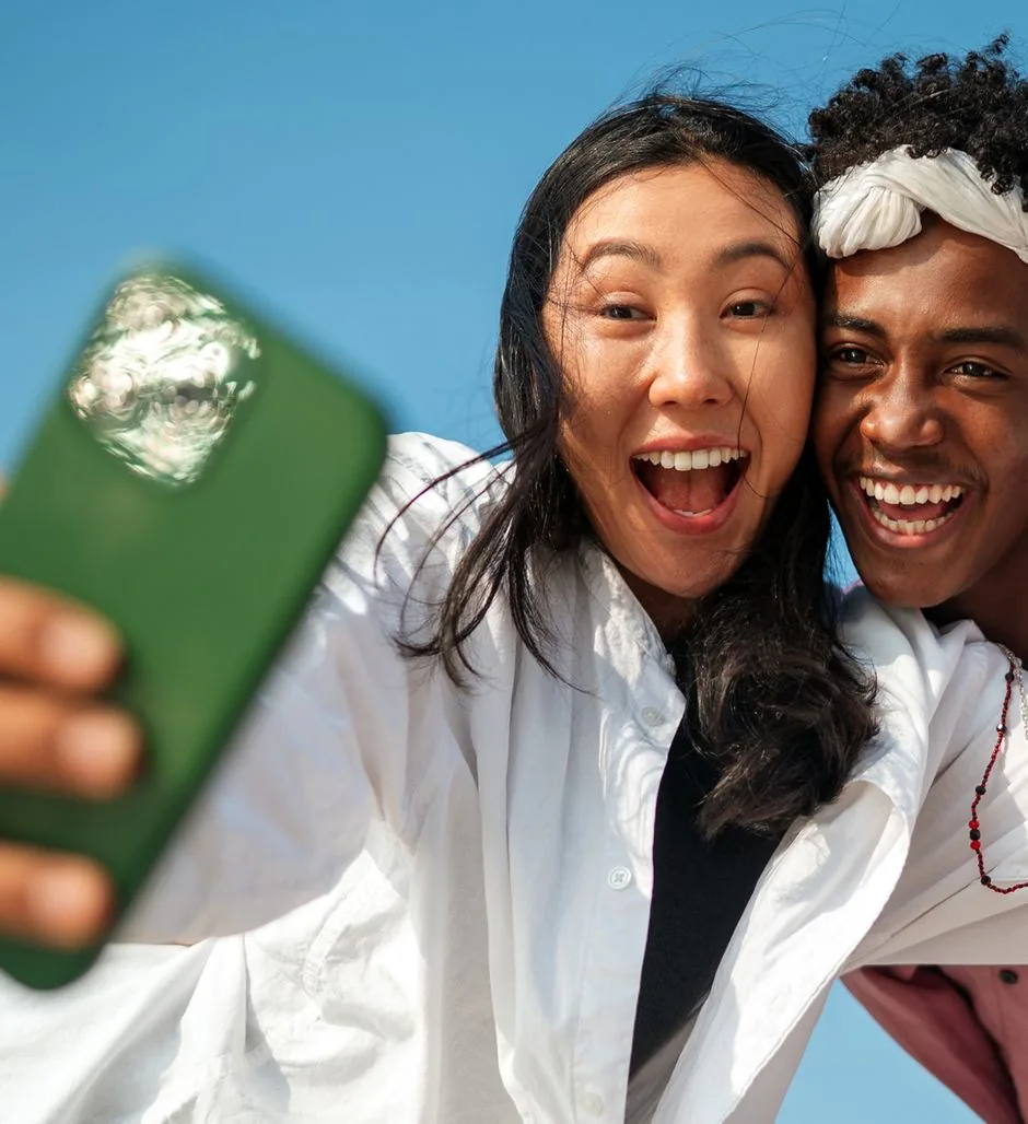 Two friends laughing as they take a selfie with a green phone