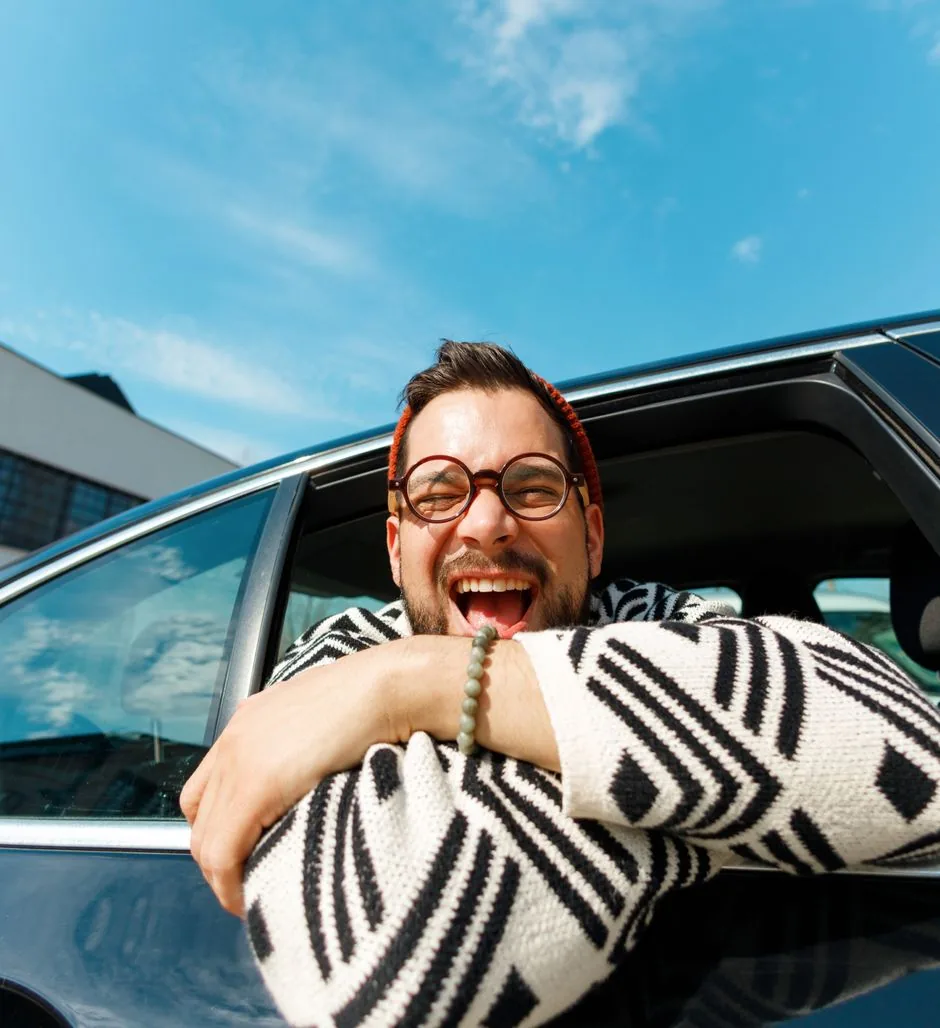 Man in round glasses laughing as he leans out of a car window