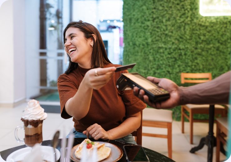 A smiling woman in a café tapping her card against a handheld payment terminal
