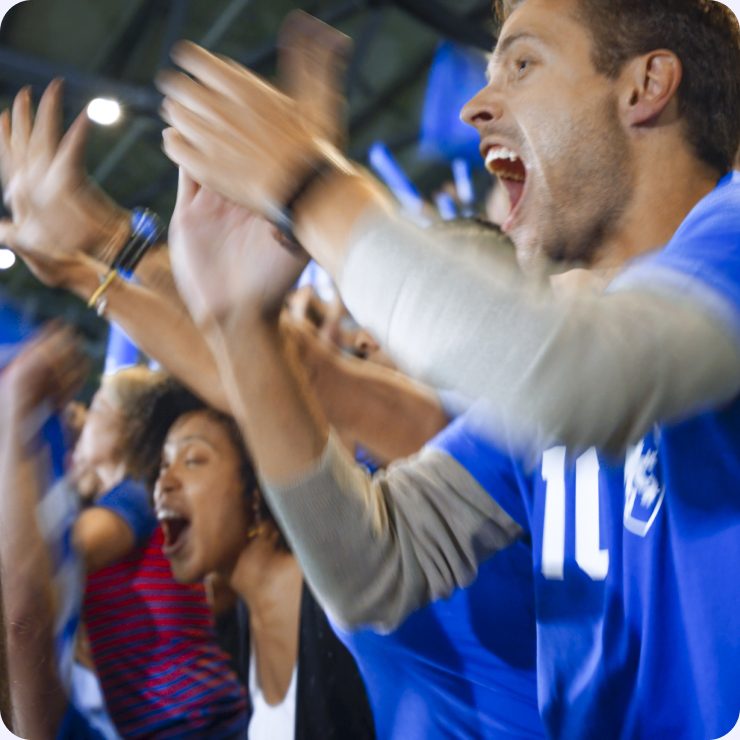 Fans in team jerseys cheering with their arms raised at a packed stadium