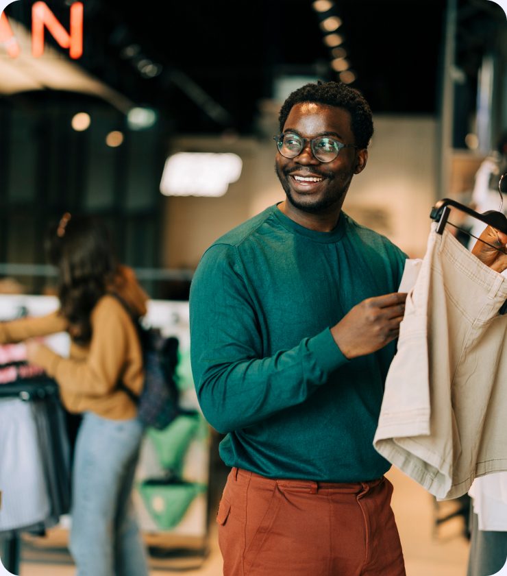 A shopper in a green sweater examining a coat on a clothing rail