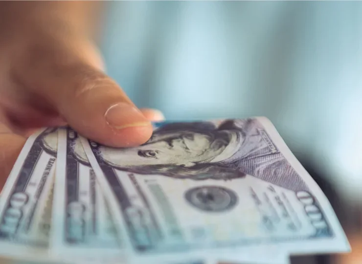 A hand holding a fan of US dollar bills