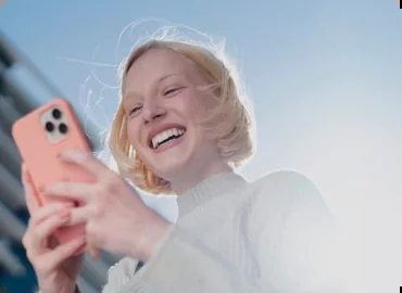 A woman laughing as she looks at her phone in a coral case