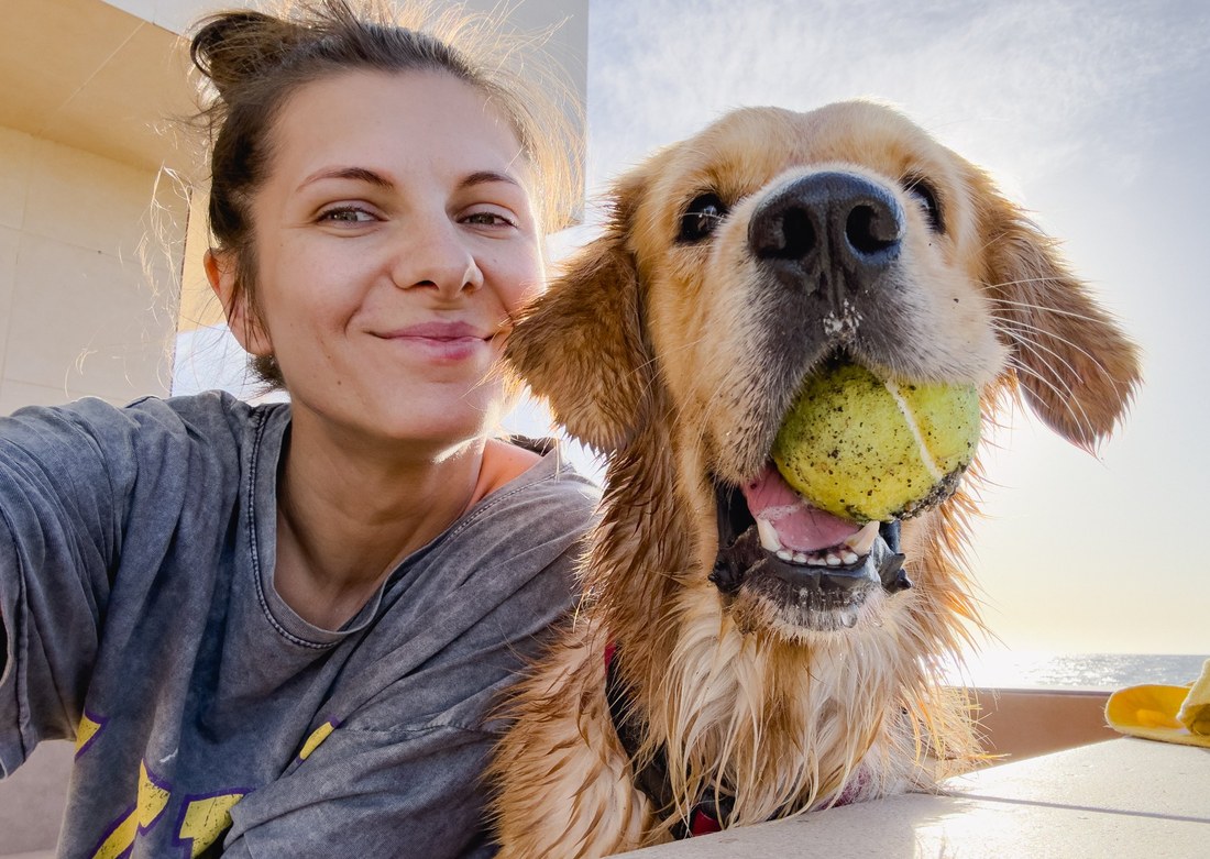 A woman taking a selfie with her golden retriever, tennis ball in its mouth