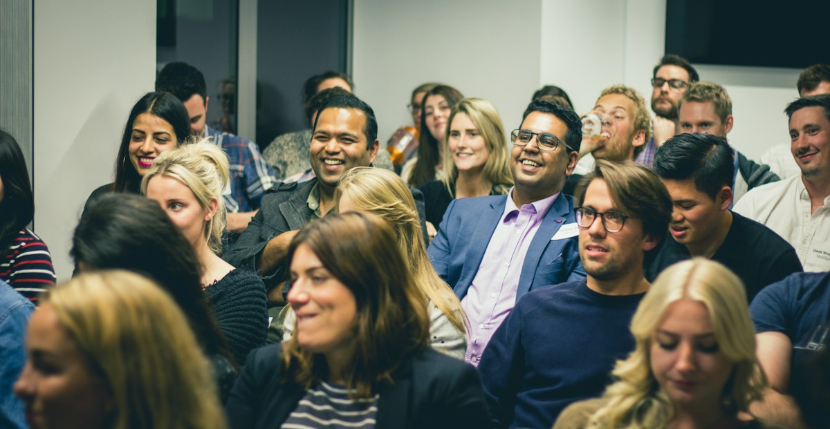 A packed seminar audience, several people laughing at something off camera.