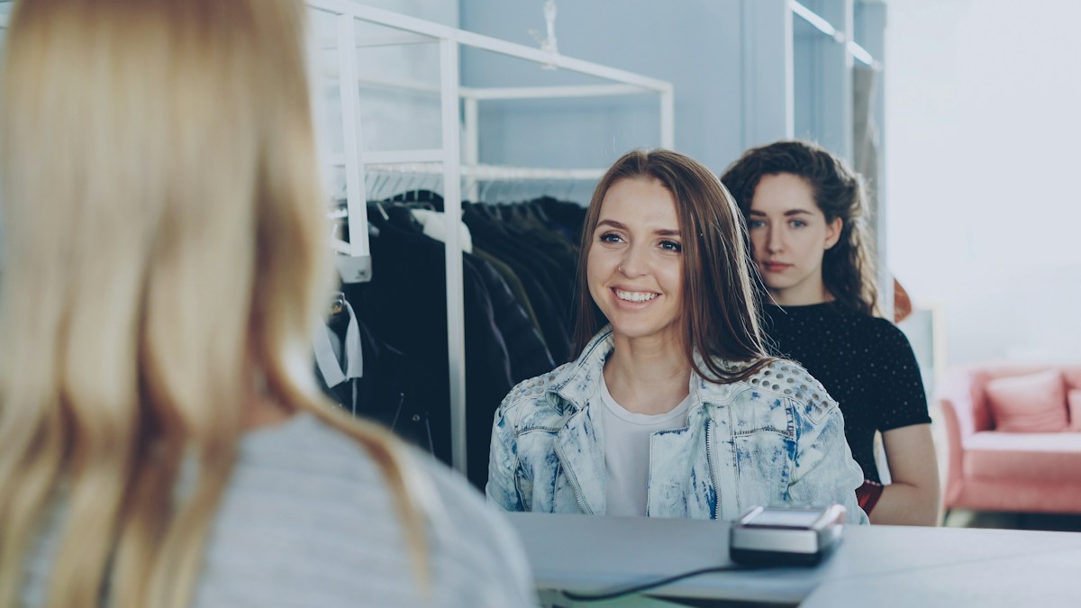 A smiling customer at a shop counter, seen over the shoulder of the assistant serving her.